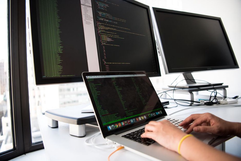 software engineer writing code on dual monitors in a bright workspace